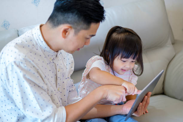 istock Father and daughter playing with digital tablet on sofa 1098355032