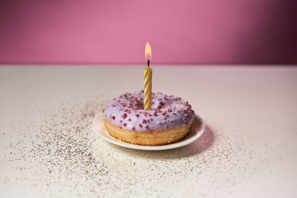 istock burning candle in middle of glazed doughnut with sparkles on white table on pink background 1098358678