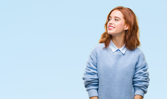 Young beautiful woman over isolated background wearing winter sweater looking away to side with smile on face, natural expression. Laughing confident.