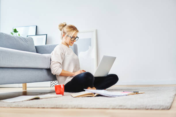 female student sitting on floor of her apartment with laptop and notes studying - education relaxation women home interior imagens e fotografias de stock