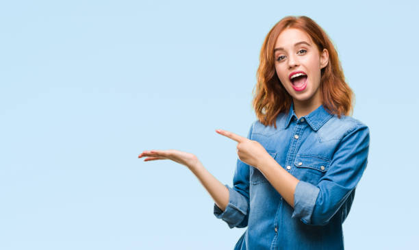 Young beautiful woman over isolated background amazed and smiling to the camera while presenting with hand and pointing with finger.