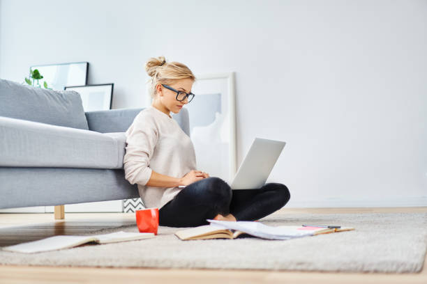 istock Young woman sitting on floor at home working with laptop and documents 1098365012