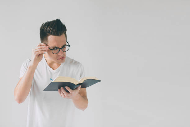 istock nerd with glasses and a white t-shirt is reading a book on a white background 1098366400