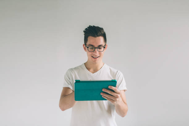 istock Nerd is wearing glasses holds the white empty screen tablet device. A man in a white T-shirt is standing on a white background 1098366532