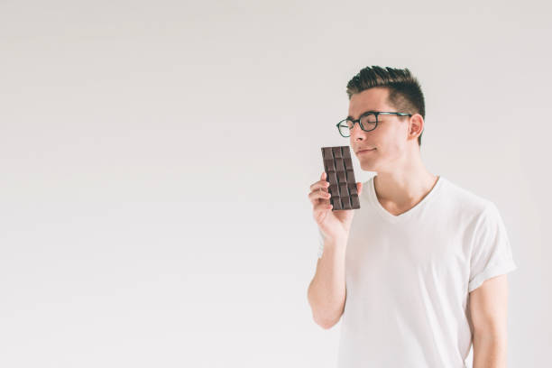 istock young man eating a chocolate bar. Nerd is wearing glasses. 1098366662