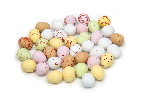 Selection of multi coloured pastel mini eggs representing Easter, on a white background.