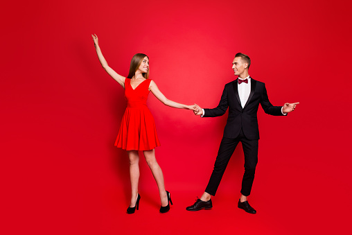 Full length body size portrait of two graceful slim attractive cheerful people looking at each other holding hands having fun dancing evening romantic isolated over bright vivid shine red background