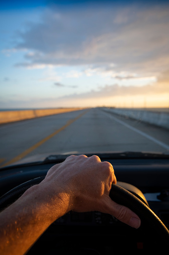 Hand of a driver on the steering wheel while driving on a two-lane highway at sunrise in the Florida Keys. Open road and copyspace.