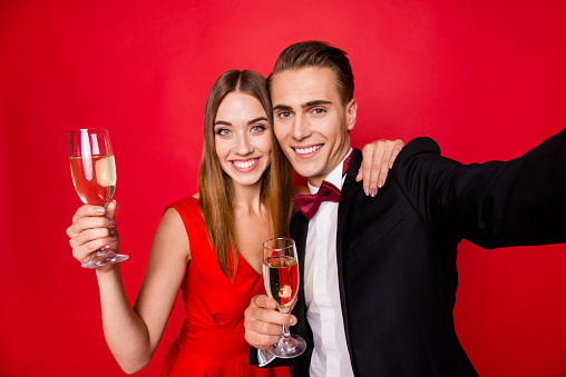 Self-portrait of two nice lovely attractive gorgeous cheerful positive people holding in hands glasses new year xmas christmas eve noel festive isolated over bright vivid shine red background