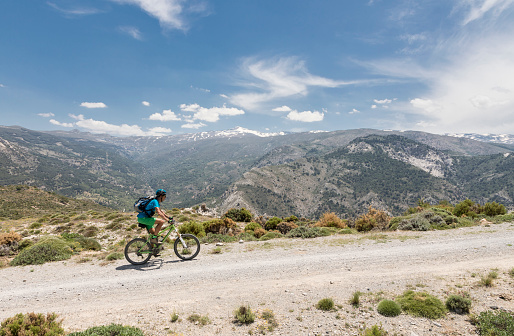 A lonely male mountainbiker is riding on a gravel road with the main range of Andalucian Sierra Nevada in the background. The the Andalucian Sierra Nevada is a mountain range in the province of Granada and, a little further, Málaga and Almería in Spain. It contains the highest point of continental Spain and the third highest in Europe after the Caucasus Mountains and the Alps, Mulhacén at 3,479 metres (11,414 ft) above sea level. 
It is a popular tourist destination. Parts of the range have been included in the Sierra Nevada National Park. The range has also been declared a biosphere reserve.
Canon EOS 5D Mark IV, 1/320, f/11, 24 mm.