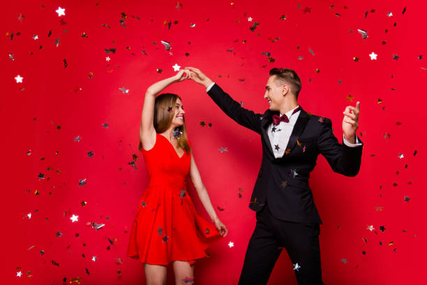 Portrait of two cool slim graceful adorable imposing attractive Portrait of two cool slim graceful adorable imposing attractive cheerful people friends rejoicing flying decorative elements glitter having fun isolated over bright vivid shine red background prom fashion stock pictures, royalty-free photos & images