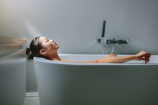 Young woman relaxing in bathtub. Asian female lying in bathtub.