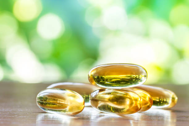 capsule di integratore di olio di pesce su tavolo di legno con sfondo naturale verde - vitamin e cod liver oil vitamin pill capsule foto e immagini stock