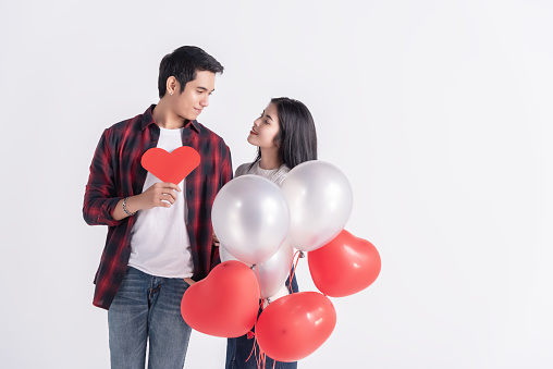 Beautiful Young couple at home,enjoy spend time together in celebration Saint Valentine's day,hand hold gift paper heart,red and white balloon,happy and love motion.