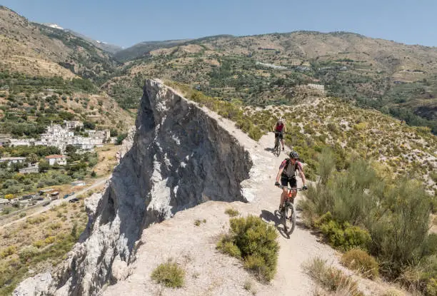 Photo of Couple of mountainbikers on a single trail nearby a cliff at Andalucian Sierra Nevada, Spain.