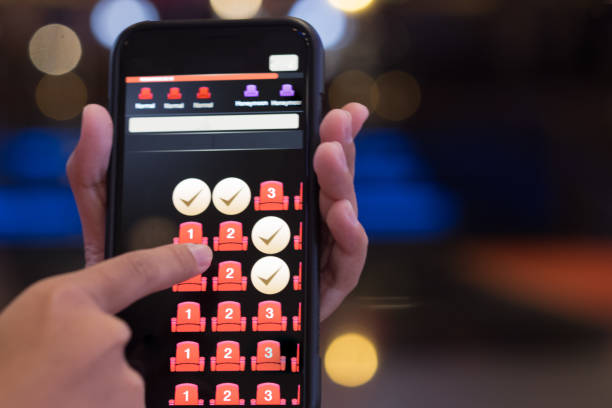 istock Hand holding smartphone with booking button and seat icon on screen. Mobile application for online buy cinema tickets. Concept of hotel booking online 1098390256