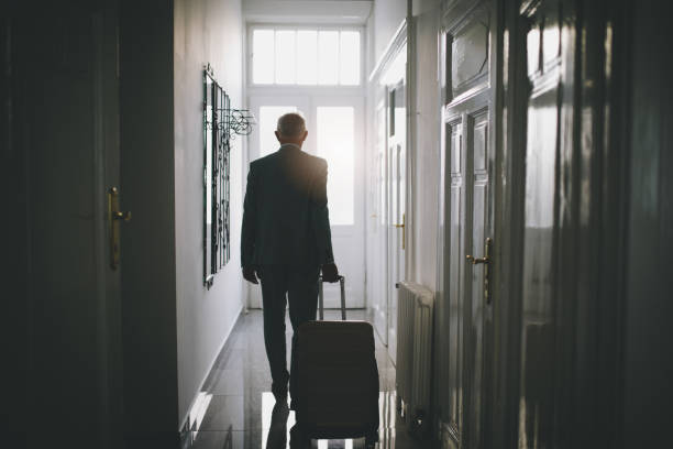 Senior businessman leaving his hotel room Fashionable senior businessman in suit, leaving his hotel apartment packet with a suitcase. disembarking stock pictures, royalty-free photos & images