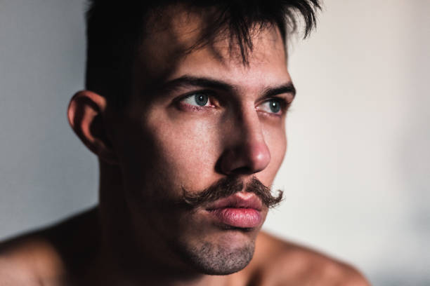istock Young shirtless man with mustache thinking by the window 1098391614