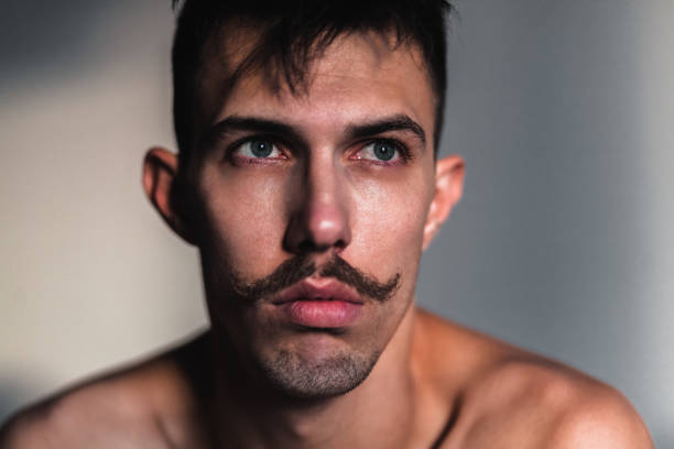 istock Young shirtless man with mustache thinking by the window 1098391632