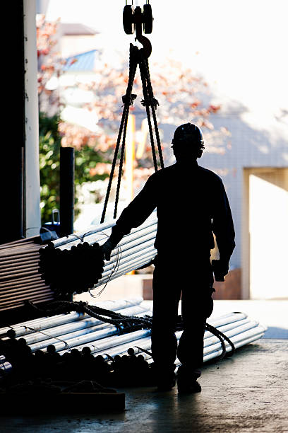 Industrial Worker Moving Metal Pipes With Crane In Warehouse Silhouette of industrial worker moving metal pipes with a industry crane in Warehouse. factory worker silhouette stock pictures, royalty-free photos & images