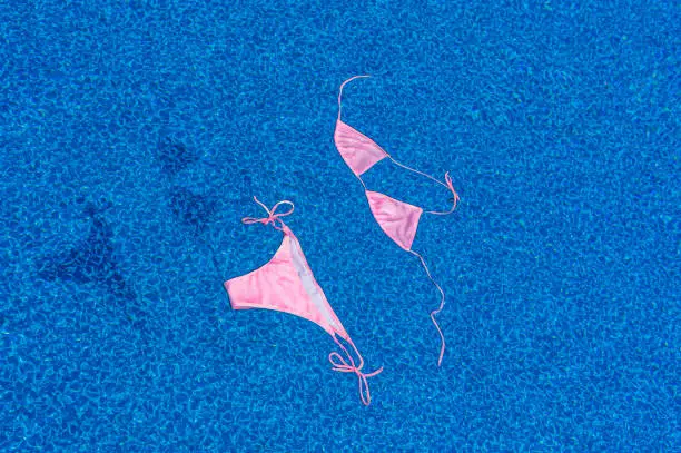 An empty pink string bikini floating on top of the water of a swimming pool with no one around. Concept freedom