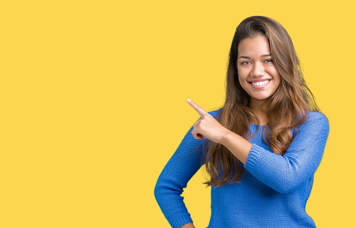 Young beautiful brunette woman wearing blue sweater over isolated background Pointing with hand finger to the side showing advertisement, serious and calm face