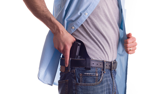 Stock photo of a man drawing a concealed carry pistol from a waist band holster.