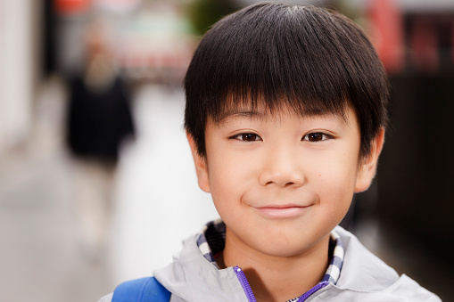 A Japanese boy standing on a sidewalk in downtown Tokyo.