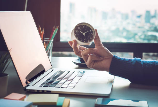 ラップトップ コンピューター上の時計が保持しているビジネスマンとのビジネスの概念。投資分析の成功を待っています。 - clock time business waiting ストックフォトと画像