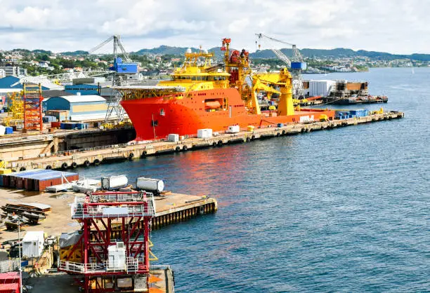 Photo of A large orange and yellow colored Offshore Construction Vessel (OCV) is in a dry dock of a shipyard and is being repaired