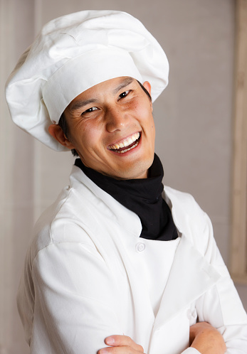 A happy Japanese man wearing a chef uniform.