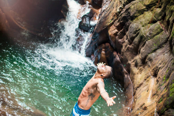 Latin man who opens his arms before the beautiful nature that gives the water of the beautiful waterfall while looking at the sky and observes a beautiful landscape.