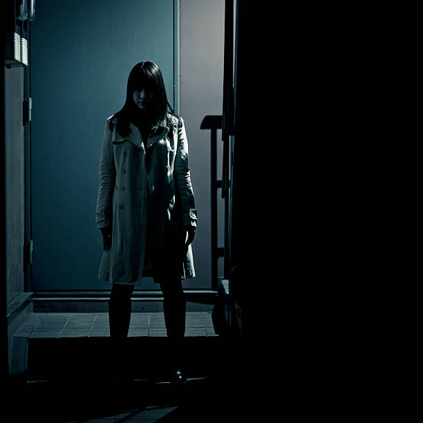 spooky japanese girl at the entrance of building stalker/spy/criminal - spooky scene were a japanese girl wearing a light colored coat appears to be waiting in the dark at the entrance of a modern building in tokyo creepy stalker stock pictures, royalty-free photos & images