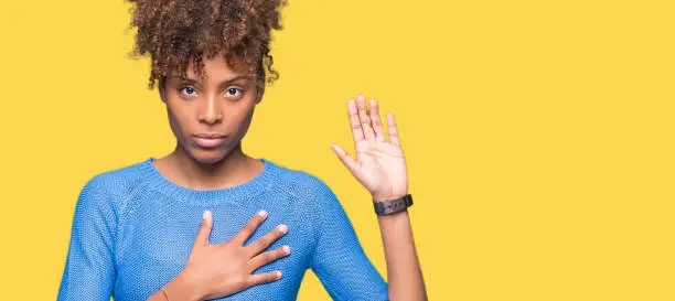 Photo of Beautiful young african american woman over isolated background Swearing with hand on chest and open palm, making a loyalty promise oath