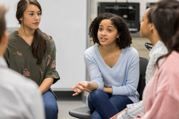 Teenage girl talks during support group meeting Mixed race teenage girl gestures while talking withe fellow teenagers during a support group meeting. teenagers only photos stock pictures, royalty-free photos & images