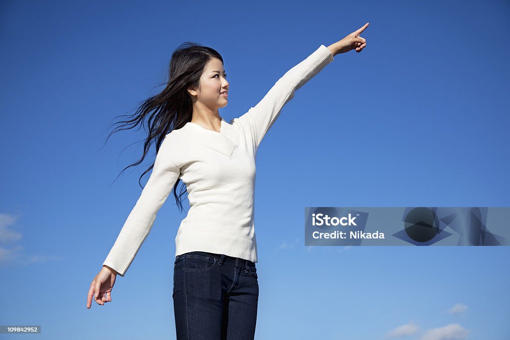 Happy woman pointing young japanese woman pointing with her finger against blue sky 20-24 Years Stock Photo