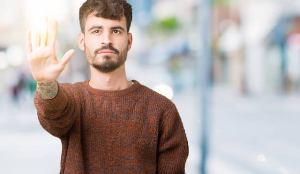 istock Young handsome man wearing winter sweater over isolated background doing stop sing with palm of the hand. Warning expression with negative and serious gesture on the face. 1098432668