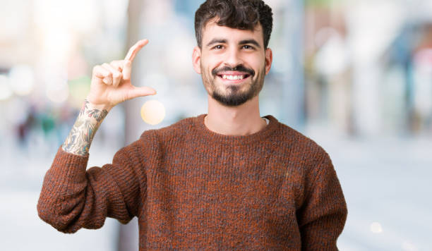 istock Young handsome man wearing winter sweater over isolated background smiling and confident gesturing with hand doing size sign with fingers while looking and the camera. Measure concept. 1098432670