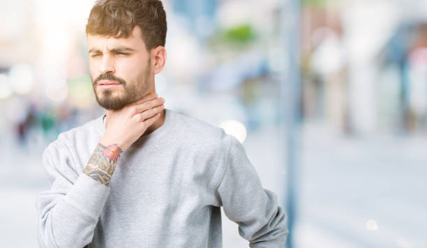 istock Young handsome man wearing sweatshirt over isolated background Touching painful neck, sore throat for flu, clod and infection 1098433656