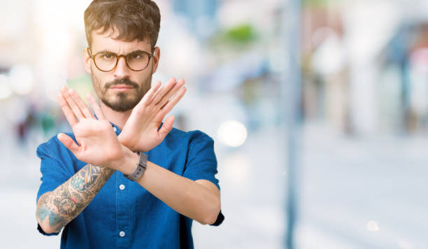 istock Young handsome man wearing glasses over isolated background Rejection expression crossing arms and palms doing negative sign, angry face 1098437234