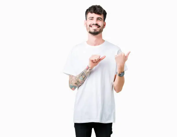 Young handsome man wearing white t-shirt over isolated background Pointing to the back behind with hand and thumbs up, smiling confident