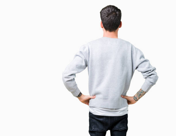 Young handsome man wearing sweatshirt over isolated background standing backwards looking away with arms on body Young handsome man wearing sweatshirt over isolated background standing backwards looking away with arms on body body adornment rear view young men men stock pictures, royalty-free photos & images