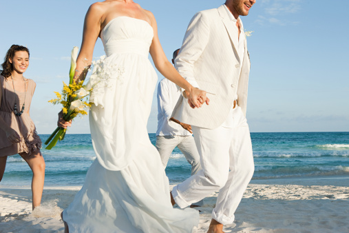 Young bride and groom happily run by the sea in their wedding clothes.