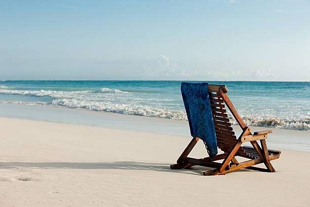 deck chair on sandy beach at water's edge - outdoor chair beach chair sarong 뉴스 사진 이미지