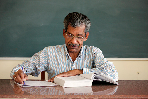 A professional businessman wearing a stylish suit and glasses is seen sitting in a comfortable chair, holding a book in his hand