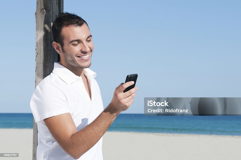 Smart phone communication Happy young man looking at news and messaging on his smart phone at beach. 20-29 Years Stock Photo