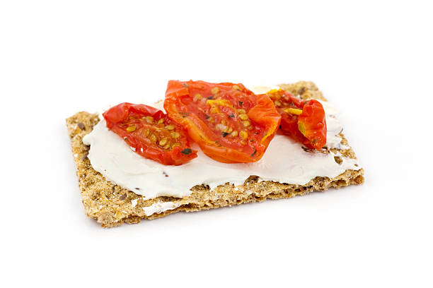Healthy snack from wholegrain rye crispbread cracker with Cherry tomatoes, salad and soft cheese on black background