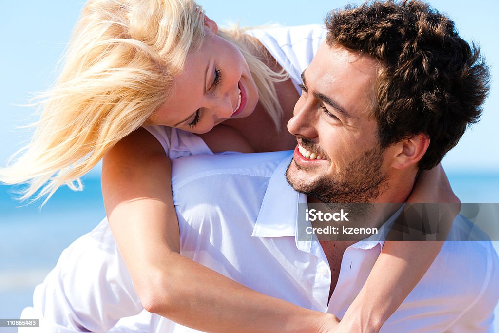 A couple in love and smiling on a summer beach Couple in love - Caucasian man having his woman piggyback on his back under a blue sky on a beach Beach Stock Photo