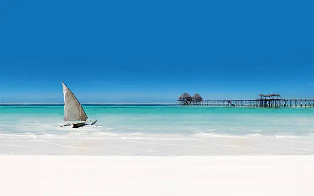 sail boat in the sea beside the white sandy beach with pier and blue skies