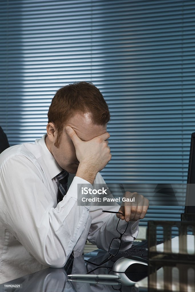 Fatigué homme dans le bureau - Photo de Se tenir la tête entre les mains libre de droits